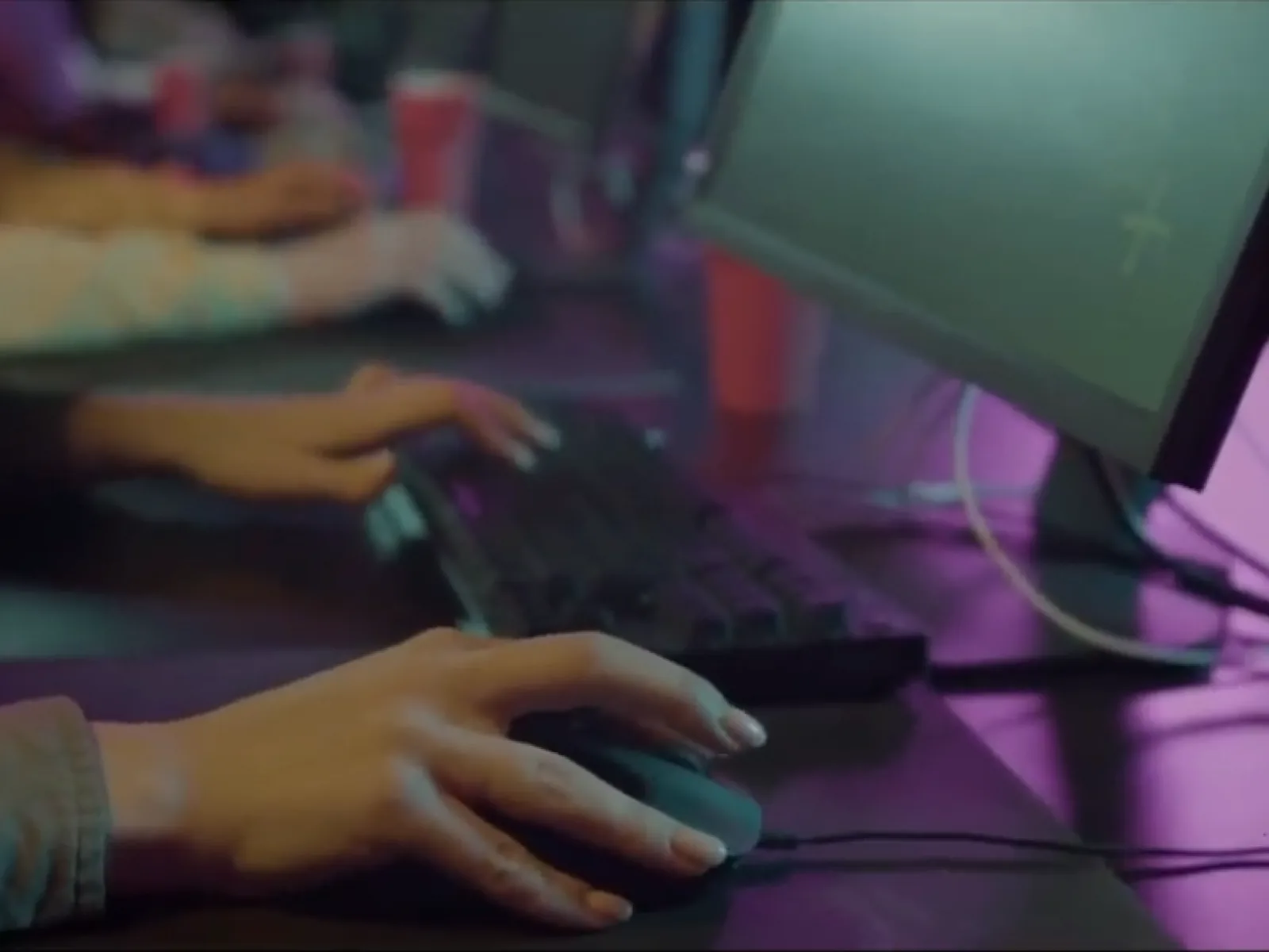 Hands on a keyboard and mouse in a dark room lit purple